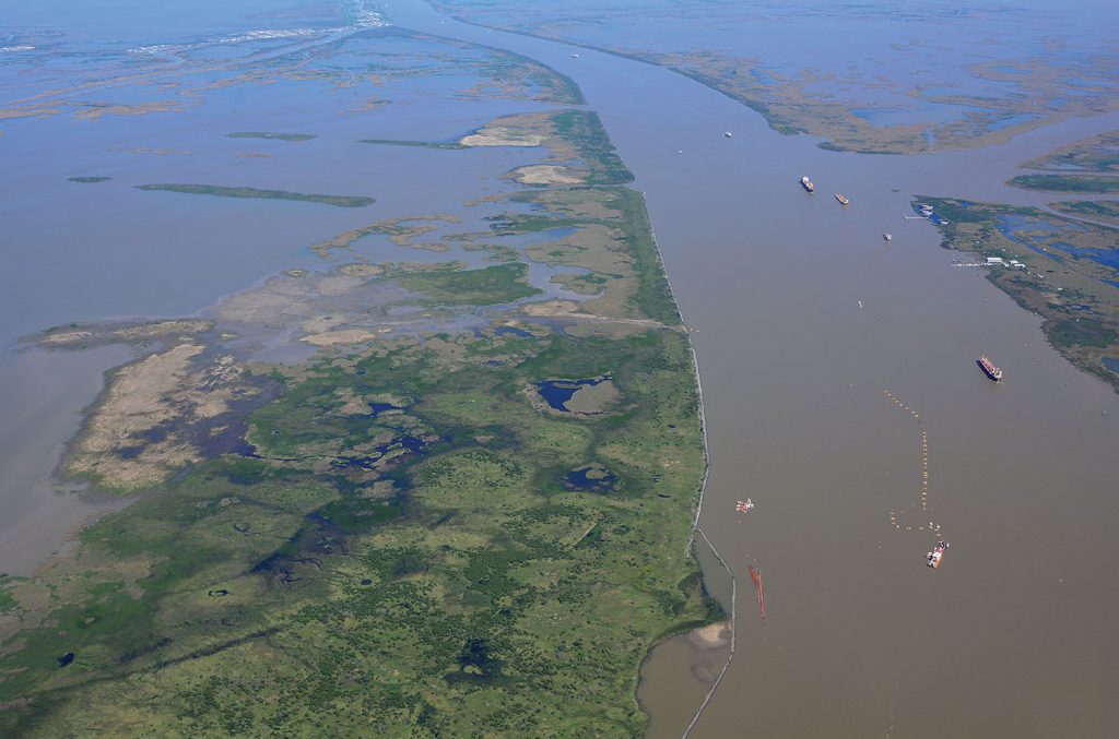 Looking upriver, a cutterhead dredge is working in the ship channel at Head of Passes, pumping into the West Bay receiving area on the left. Ship traffic has room to navigate around the stationary dredge plant. Pilot Town is visible on the right. (—Photo by Patrick Quigley, www.gulfcoastairphoto.com)