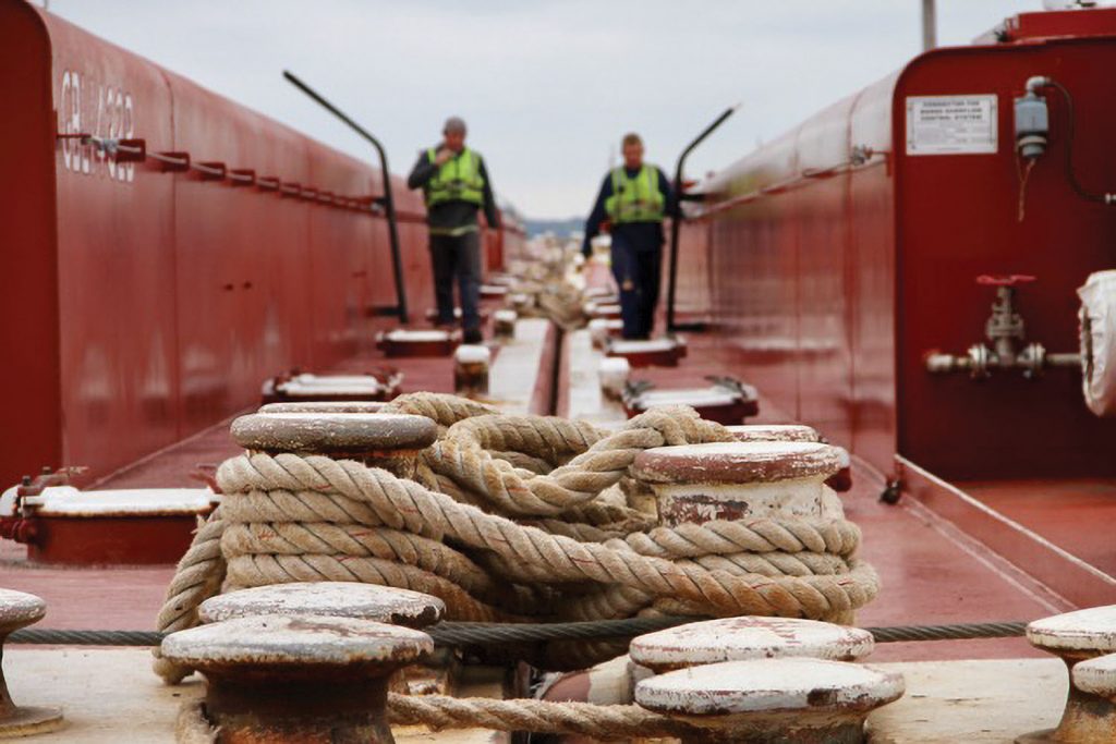 "Deckhands walking the gunnels on barges back toward the towboat after checking the tow on mv. Austin Golding," by Melody Golding