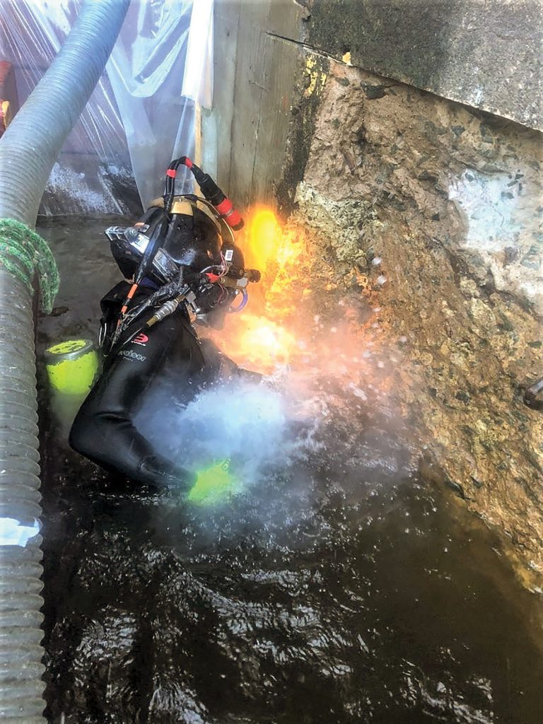 Paul Hovenga chips concrete using a rivet buster on a job in St. Croix Falls, Wis., that requires working both above and below the waterline. (Photo courtesy of J.F. Brennan Inc.)