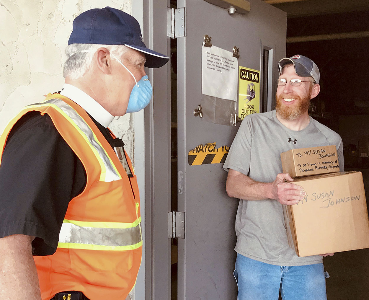 In a pastoral response adapted to the realities of the global pandemic, Senior River Chaplain Kempton Baldridge transfers two parcels to Brandon Land, supervisor at Ingram Barge Company‘s warehouse in Paducah, Ky., for further delivery to an Ingram towboat crew on the Lower Mississippi River. With all vessel visits curtailed, chaplains must communicate their care and concern for crews by different means. Thus, after learning of a crewmember’s death earlier in the day, Chaplain Baldridge packed up the flag of the U.S. Merchant Marine to fly in the mariner’s memory and a large morale box loaded with books, DVDs, dental kits, snacks and prayer books for his shipmates, ever mindful to observe “social distancing” protocols. (Photo courtesy of Seamen's Church Institute)