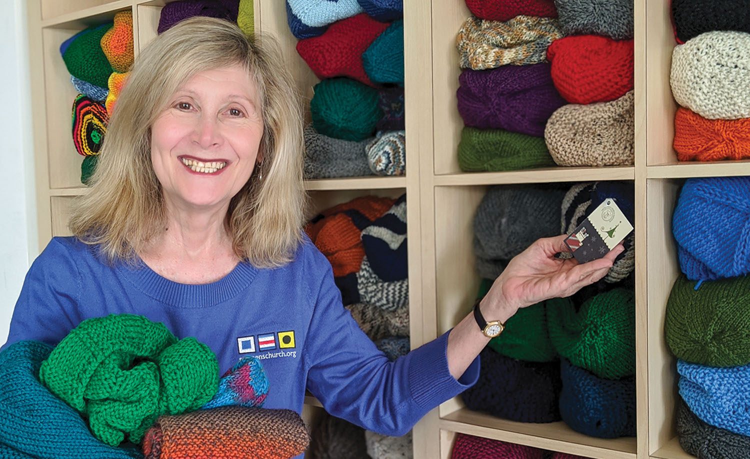 Joanne Bartosik, manager of Seamen’s Church Institute’s Christmas at Sea/Christmas on the River program, shows off some of the many knitted items SCI collects to give out as Christmas gifts to mariners. (Photo courtesy of Seamen's Church Institute)