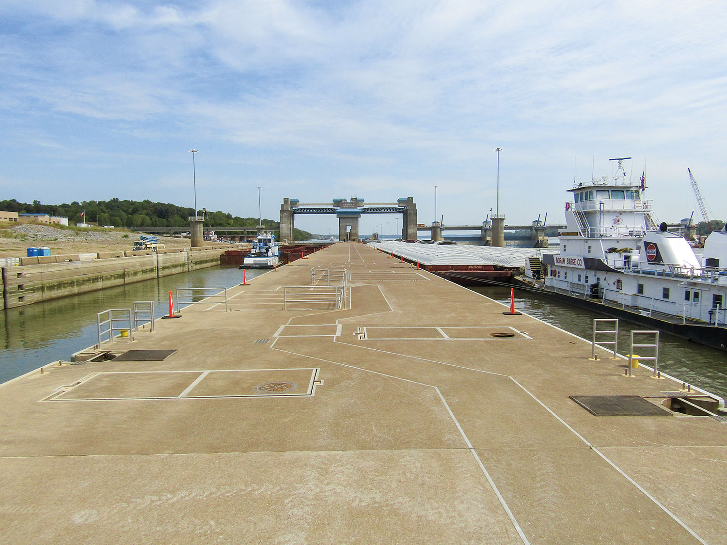 —Photo courtesy of Louisville Engineer District Two upbound tows lock through at Olmsted Locks and Dam in September 2019. In June, the Corps raised the wickets for the first time in 2020, the fourth time since Olmsted opened in August 2018. By Shelley Byrne River traffic has locked through the twin 1,200-foot-by-110-foot chambers at Olmsted Locks and Dam for the first time this year and only the fourth time in the project’s history. “The weather conditions over the past couple of years have been unique, but raising it in June is much more normal,” said Ryan Lawrence, assistant operations manager for the Louisville Engineer District’s locks and dams project office. Olmsted personnel began raising the wicket dam June 18. It had also been raised in August 2018, August 2019 and November 2019, for a total of about 100 days, Lawrence said. The longest period was in August 2019, when the wicket dam held pool for 62 days at 301.5 feet above sea level, maintaining the pool 46 river miles, back to the Smithland Locks and Dam. A more typical elevation at Olmsted is 295 to 300 feet, based on a hinged pool that takes advantage of the natural slope of the river. Crews began lowering the wickets June 23 in response to rainfall in the upper Ohio Valley, but Lawrence said they may need to go back up again in another two weeks or so, given current forecasting that calls for less rain and a falling Mississippi River. The Corps said it expects to raise and lower the wickets an average of four times each season. “But so far we haven’t really had an average year,” Lawrence said. “You do what needs to be done to maintain the river elevations.” Given the weather so far this year, the Corps believes this season may be much closer to a typical one than the last two have been. However, Lawrence cautioned, “As we saw last year, there’s no real way to know. We look at historical trends and what we expect with weather patterns.” Although the Corps had plenty of experience with wickets at the former Locks and Dams 52 and 53, Olmsted modernized the process when it opened in August 2018 on the Ohio River near Olmsted, Ill. In addition, instead of a hook blindly grabbing for a bar on the wickets beneath the water, GPS and a sonar camera aid the process. “They really took the things they learned from 52 and 53 and implemented and improved those things here,” Lawrence said. The Corps has less experience using tainter gates combined with a wicket dam to control flow. Olmsted has five tainter gates, while the former projects didn’t have any, although other Ohio River locks and dams in the district have them. The gates can be opened and closed to maintain the pool without raising and lowering the wickets as frequently. “We’re definitely still learning that,” Lawrence said, adding that Olmsted has a unique combination of factors since high water on the Mississippi River can back up the Ohio to as far as Olmsted and since levels on Kentucky Lake on the Tennessee River, Lake Barkley on the Cumberland River and on the Ohio at Smithland