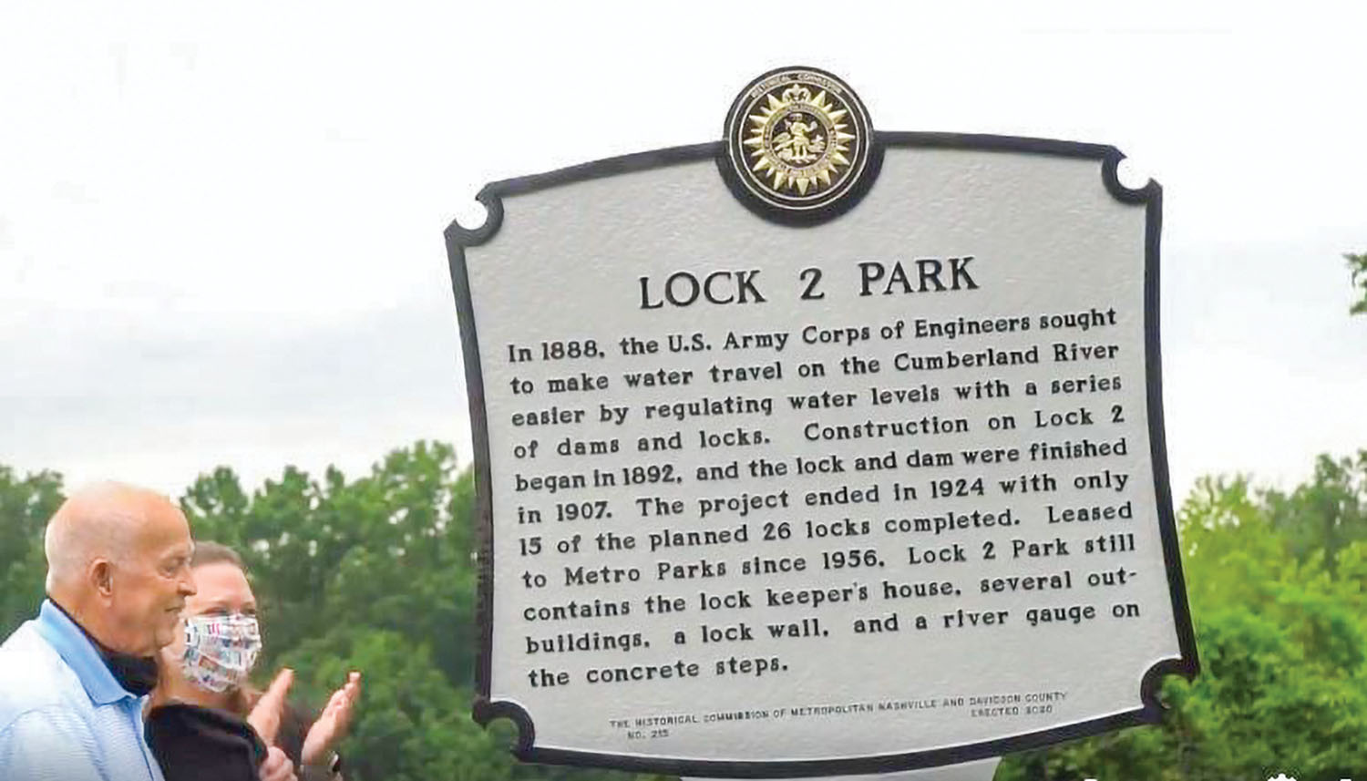 Bill Holman smiles and Jessica Reeves of the Metro Historical Commission claps moments after the historical marker at Lock 2 Park is unveiled. (Screenshot from Nashville Engineer District video)