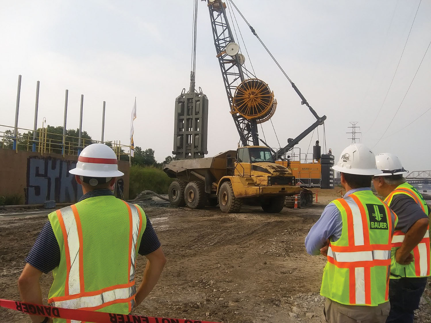 Members of the project team for the East St. Louis seepage wall project look on as a Bauer MC-96 rig in a clamshell configuration removes subsoil on the east bank of the Mississippi River just north of downtown St. Louis. The seepage wall, due to be completed in the fall of 2022, is the largest project of its type and will protect the levee system against under-seepage. (Photo by David Murray)