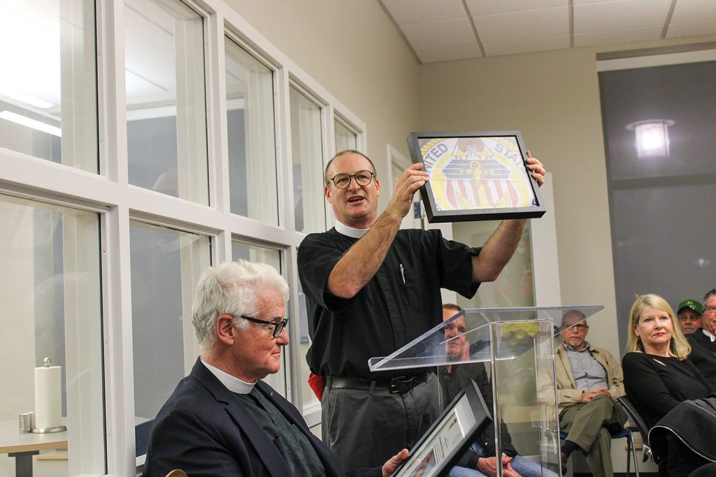 The Rev. Tom Rhoades presents the Rev. Kempton Baldridge with his own merchant mariner flag. As river chaplain, Baldridge had presented the flags to crews upon vessel christenings many times over the years. Baldridge retired as the Seamen’s Church Institute’s senior river chaplain on February 28. (Photo by Shelley Byrne)