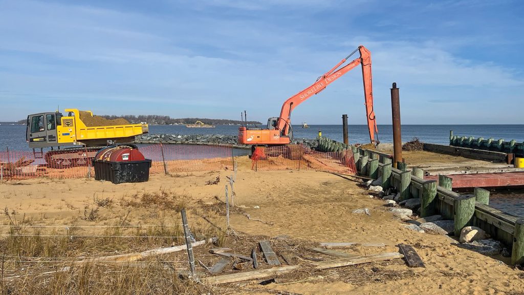 A Hitachi Longreach excavator unloads dredged sand into a 10-cubic-yard rubber-tracked dump truck, which will place the sand on the beach.
