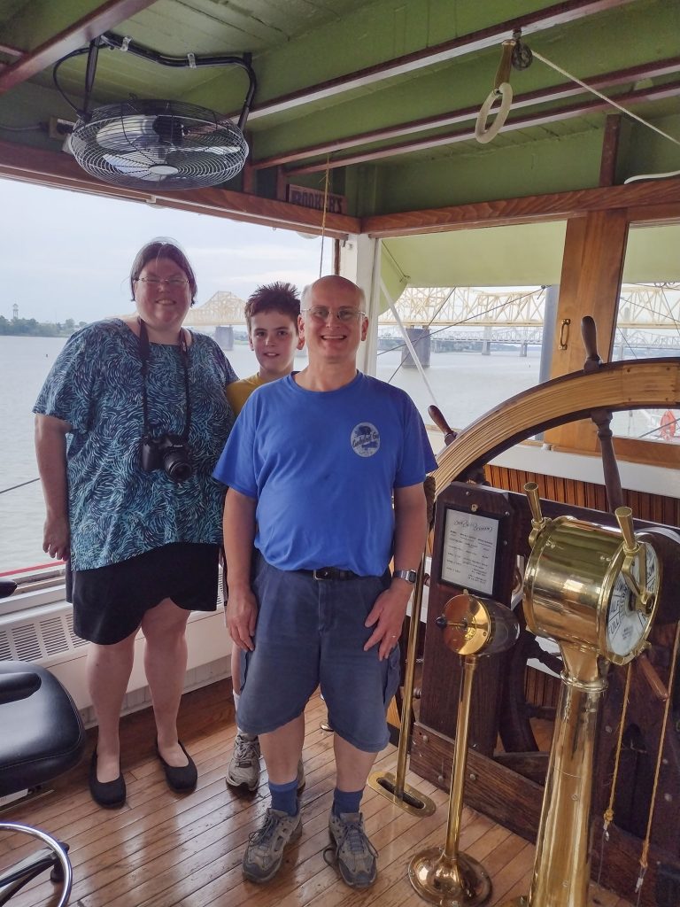 Drew Byrne, 12, and his parents, Shelley and Paul Byrne, pose by the wooden wheel in the pilothouse of the Belle of Louisville on their recent trip. (Photo by Capt. Mike Fitzgerald)