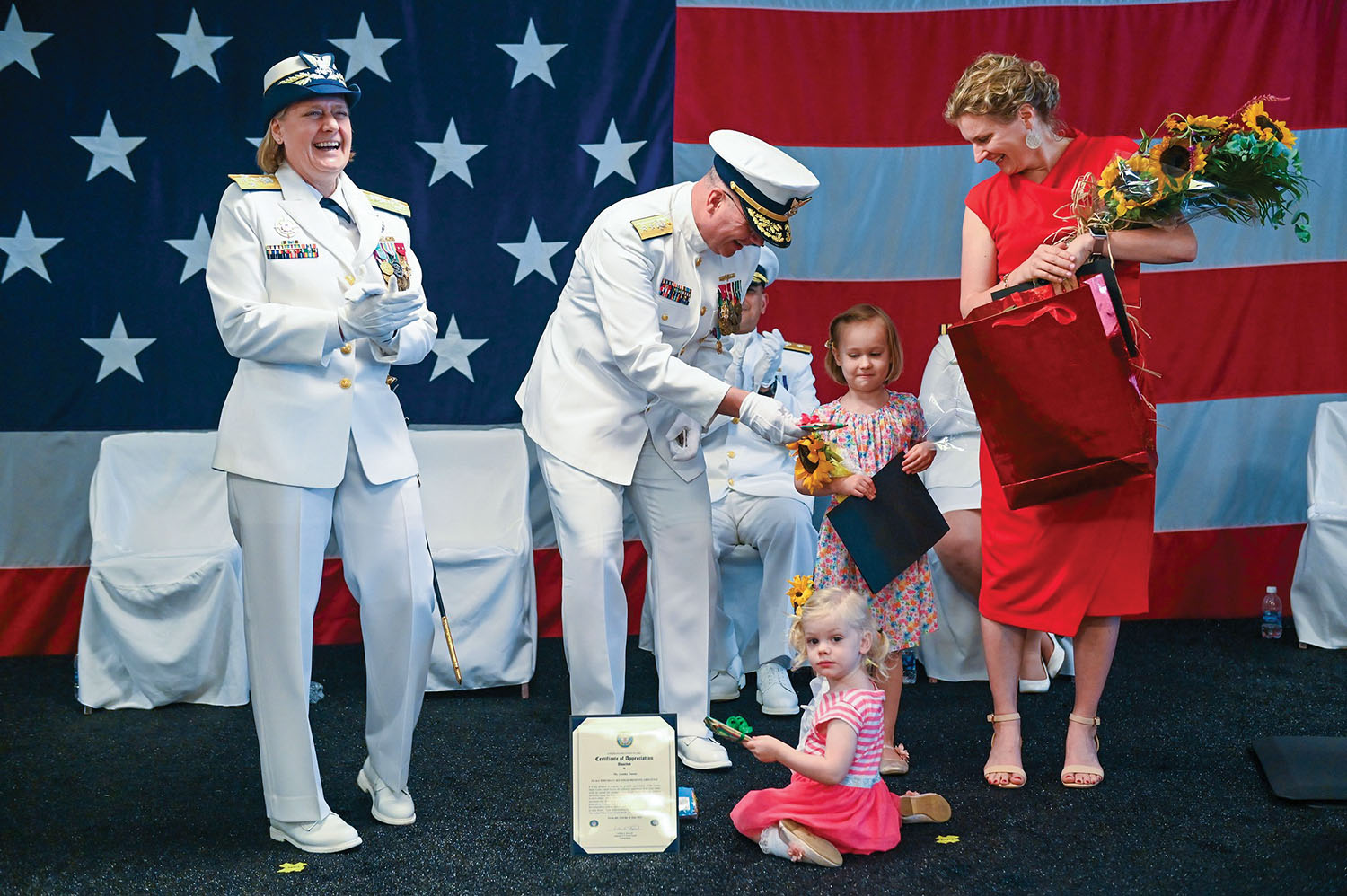 Rear Adm. Richard Timme is joined on stage during his retirement ceremony by his two daughters and his wife, Bettina. Coast Guard Commandant Adm. Linda Fagin, who led the ceremony, enjoys the moment. (Photo by Frank McCormack)