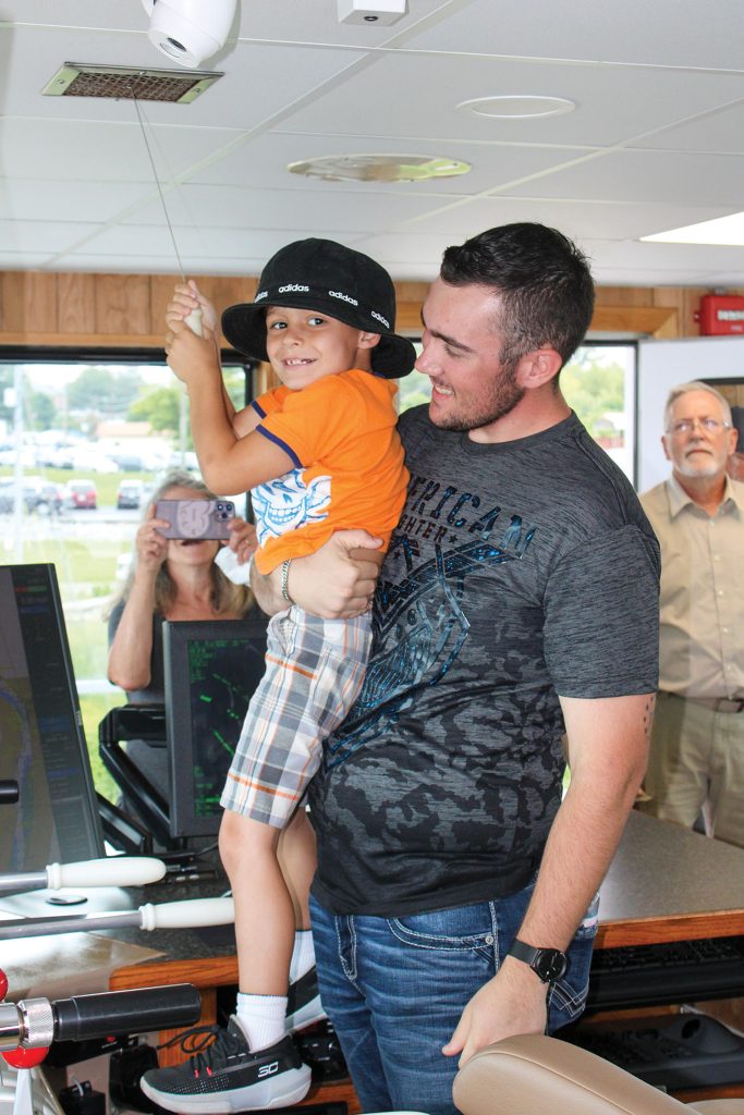 Gryffin Luenebrink, 6, of Bicknell, Ind., gets a boost from his cousin Skyler McAllum, an ARTCo fleetmate in Mount Vernon, Ind., so that he can blow the whistle of the mv. Cooperative Enterprise during an ADM/ARTCo open house. The open house, held August 12 at PTL Marine in Wickliffe, Ky., offered tours of the Cooperative Enterprise and the mv. Harvest Maiden, along with food, music and even a bounce house for employees and their families and friends. The Coast Guard also offered coloring books and a pulley game as part of their mission of ensuring safety on the water. (Photo by Shelley Byrne)