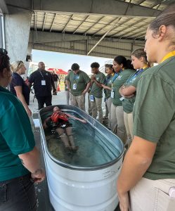 Students participate in a water rescue activity during a We Work The Waterways Maritime Interaction Day, working together to remove a lifelike rescue dummy from a training tub.